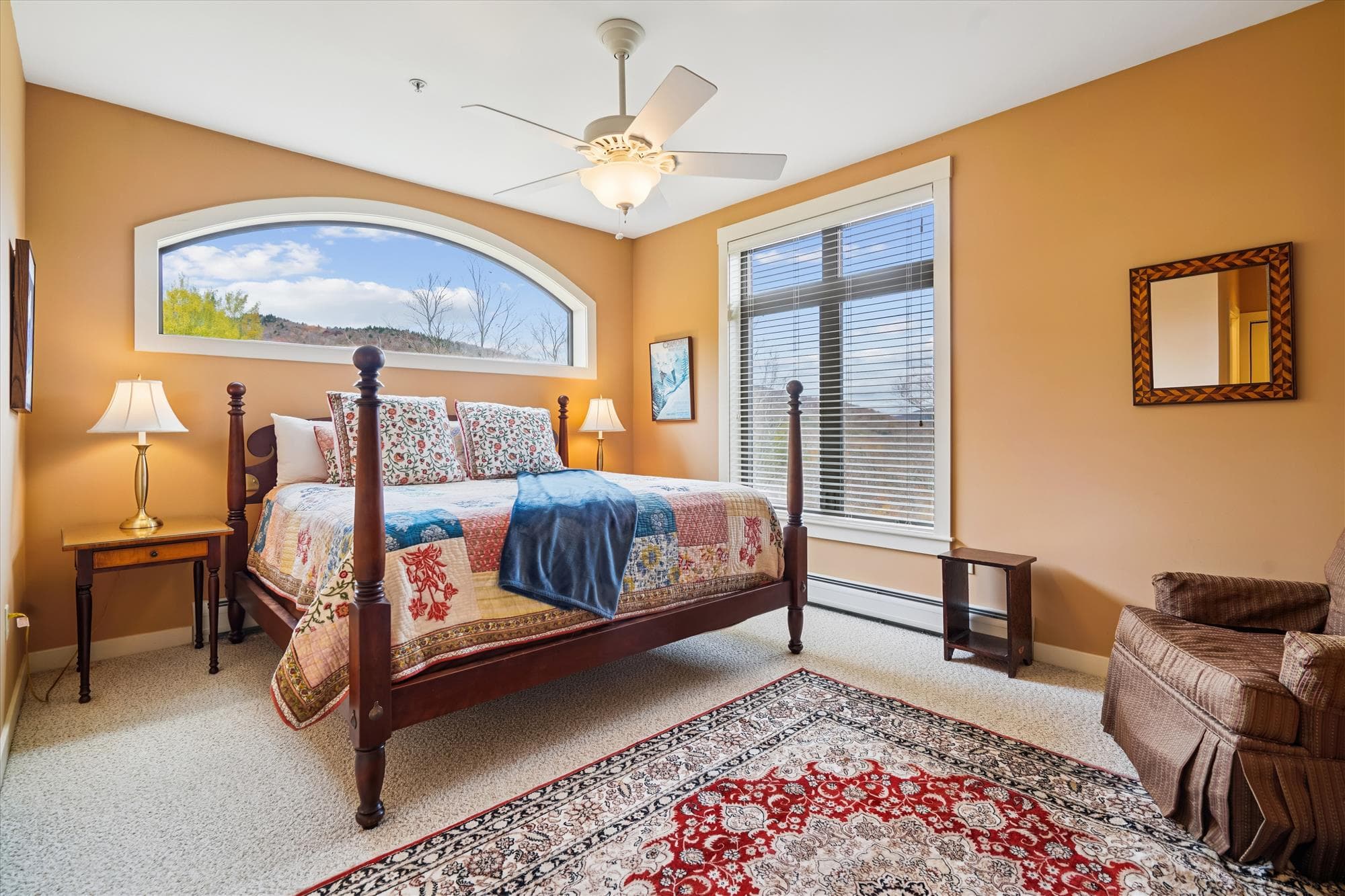 Spacious king bedroom with rich wood furnishings, a comfortable armchair, and mountain views through large windows. The warm tones and soft light make it a calm retreat after a full day on the slopes or trails.