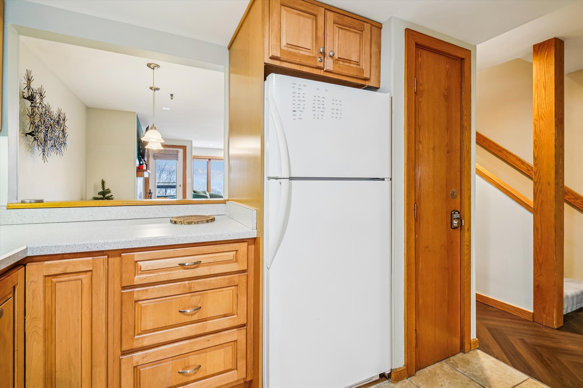 Kitchen area with full refrigerator, wood cabinetry, and a convenient breakfast bar that opens to the living space.