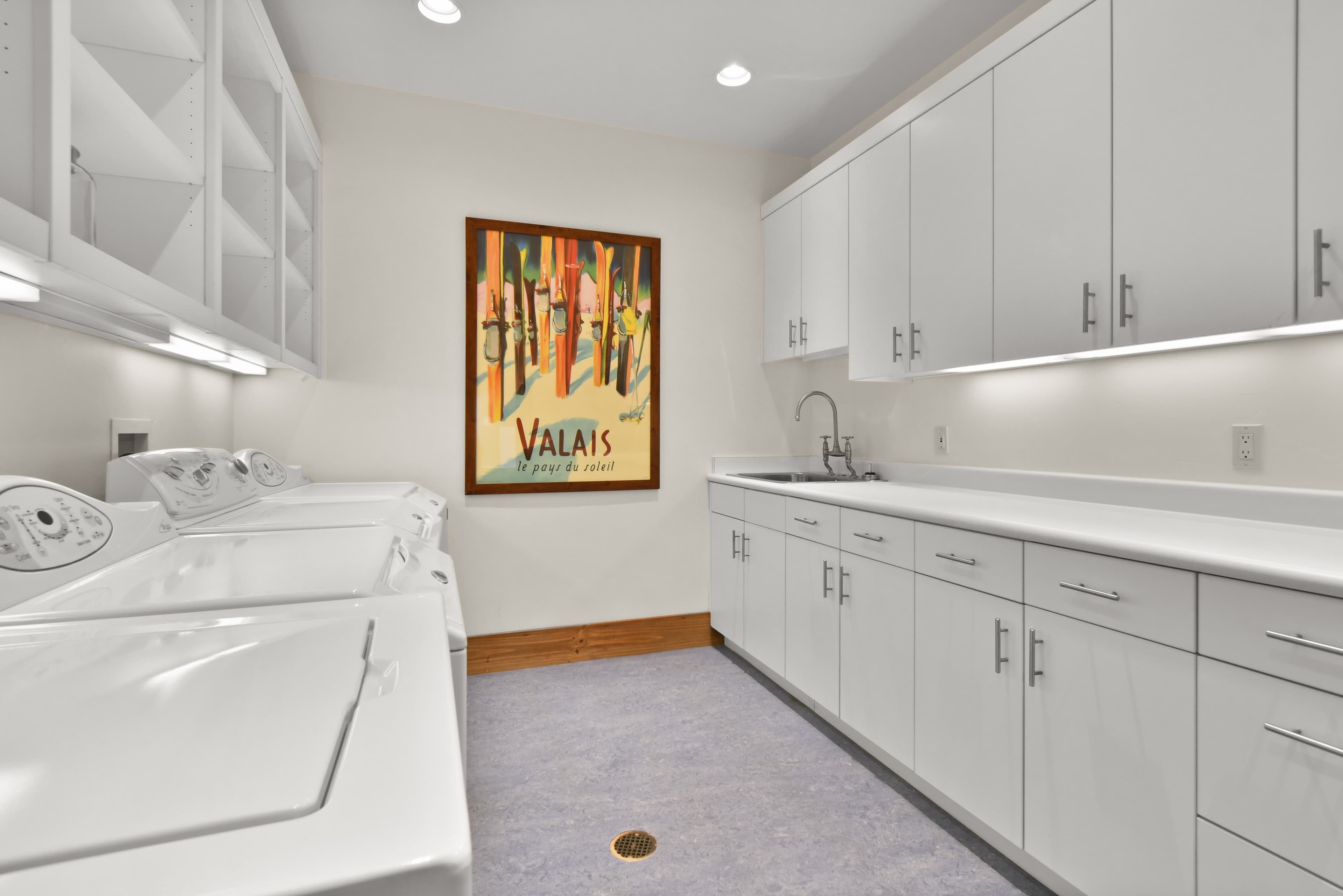 The homes laundry room, with one wall lined with washing machines and dryers, the other in cabinets.