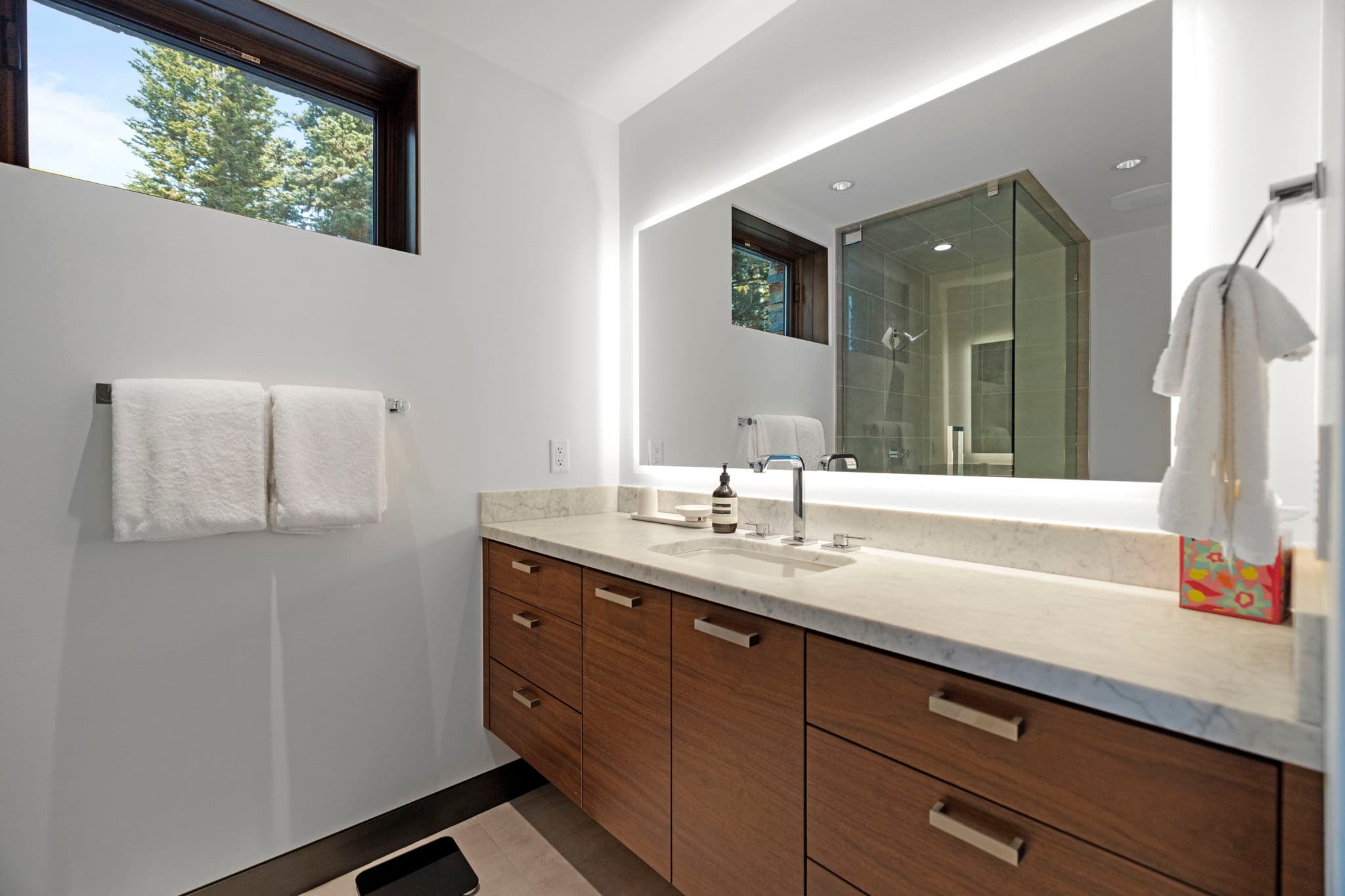 A bathroom sink with a large mirror and a window.